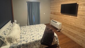A bedroom with a bed, a ceiling fan, a mounted TV, and an air conditioning unit. - The Walnut Inn, 2BR Handicap-Accessible Apt. Located in Parsons; Pet Friendly (Parsons)