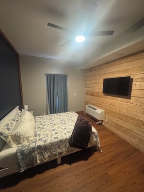 Un dormitorio con cama, ventilador de techo, televisor montado y equipo de aire acondicionado.
