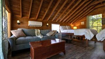 Een gezellig houten vakantiehuisje met een slaapbank, een houten salontafel, een bed en een raam met uitzicht op bomen.