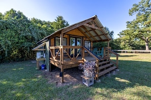 A wooden cabin with a porch, a small deck, and a fenced yard.