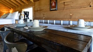 Een houten tafel gedekt met borden en bekers, een bankje en een lijst met een bordje aan de muur.