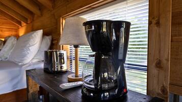 Interieur van een houten hutje met een bed, een lamp, een koffiezetapparaat en een afstandsbediening op een houten tafel.