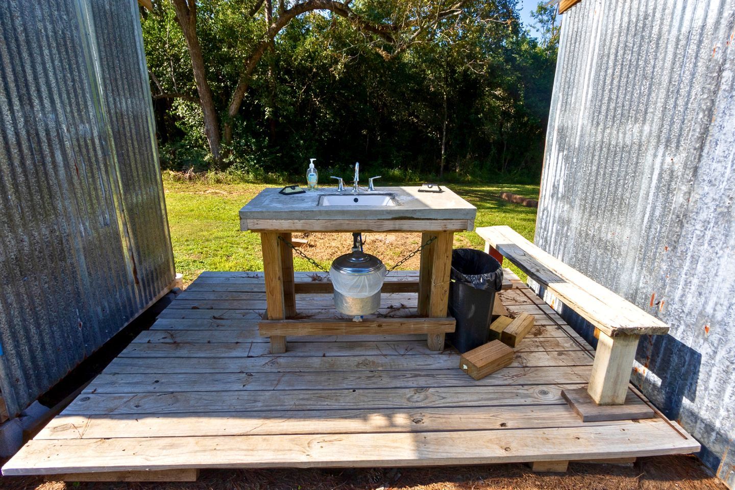 A portable outdoor kitchen with a sink, a faucet, and a trash can.