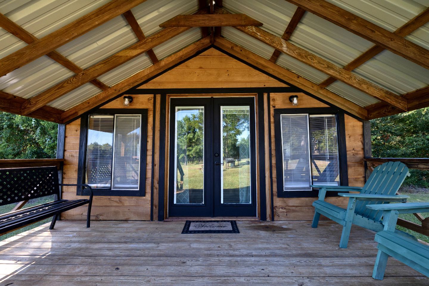 Een houten hut met een veranda, een bank en twee Adirondack-stoelen.