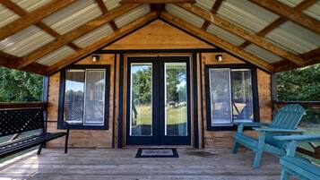Een houten hut met een veranda, een bank en twee Adirondack-stoelen.