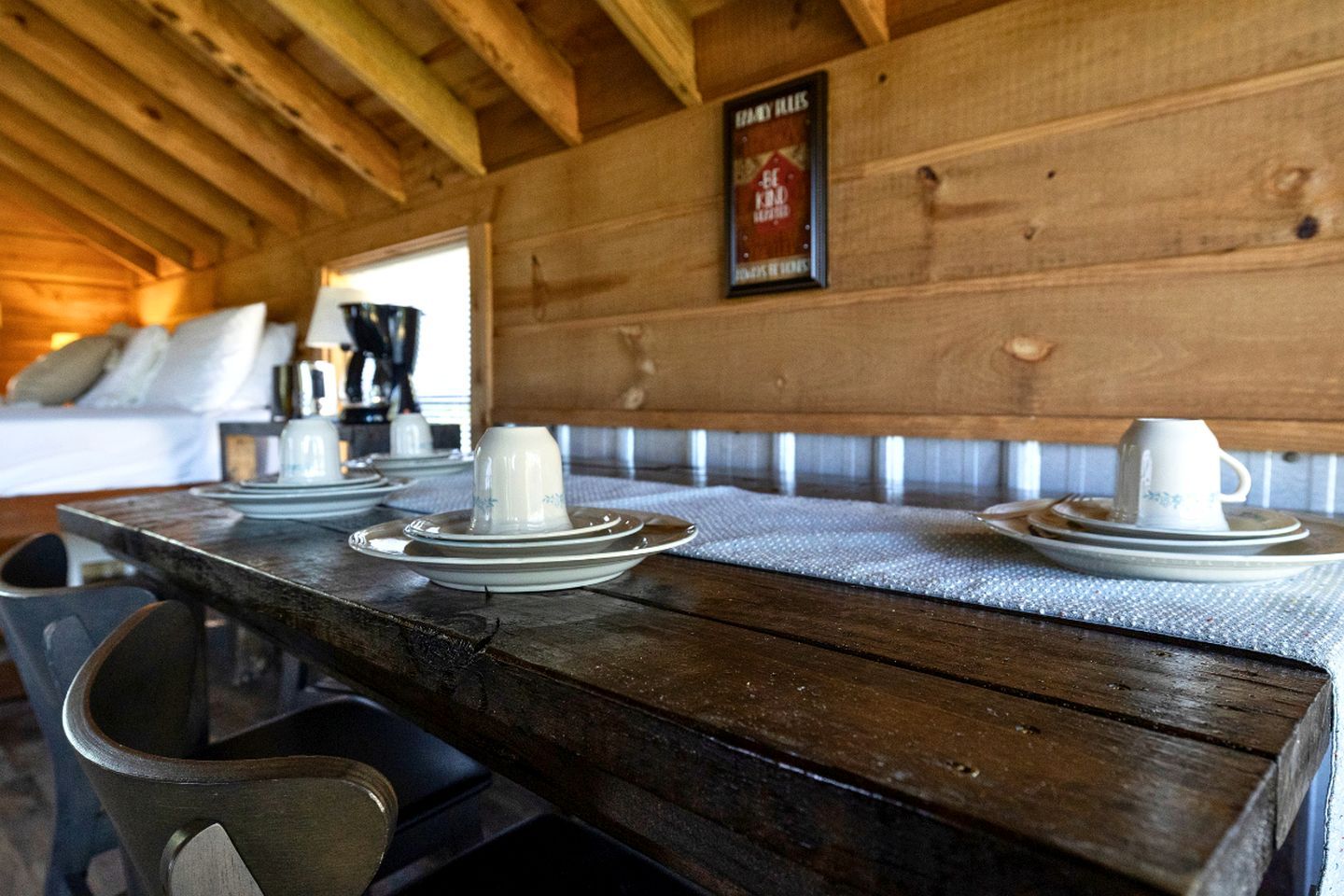 A wooden table set with plates and cups, a bench, and a framed sign on the wall.