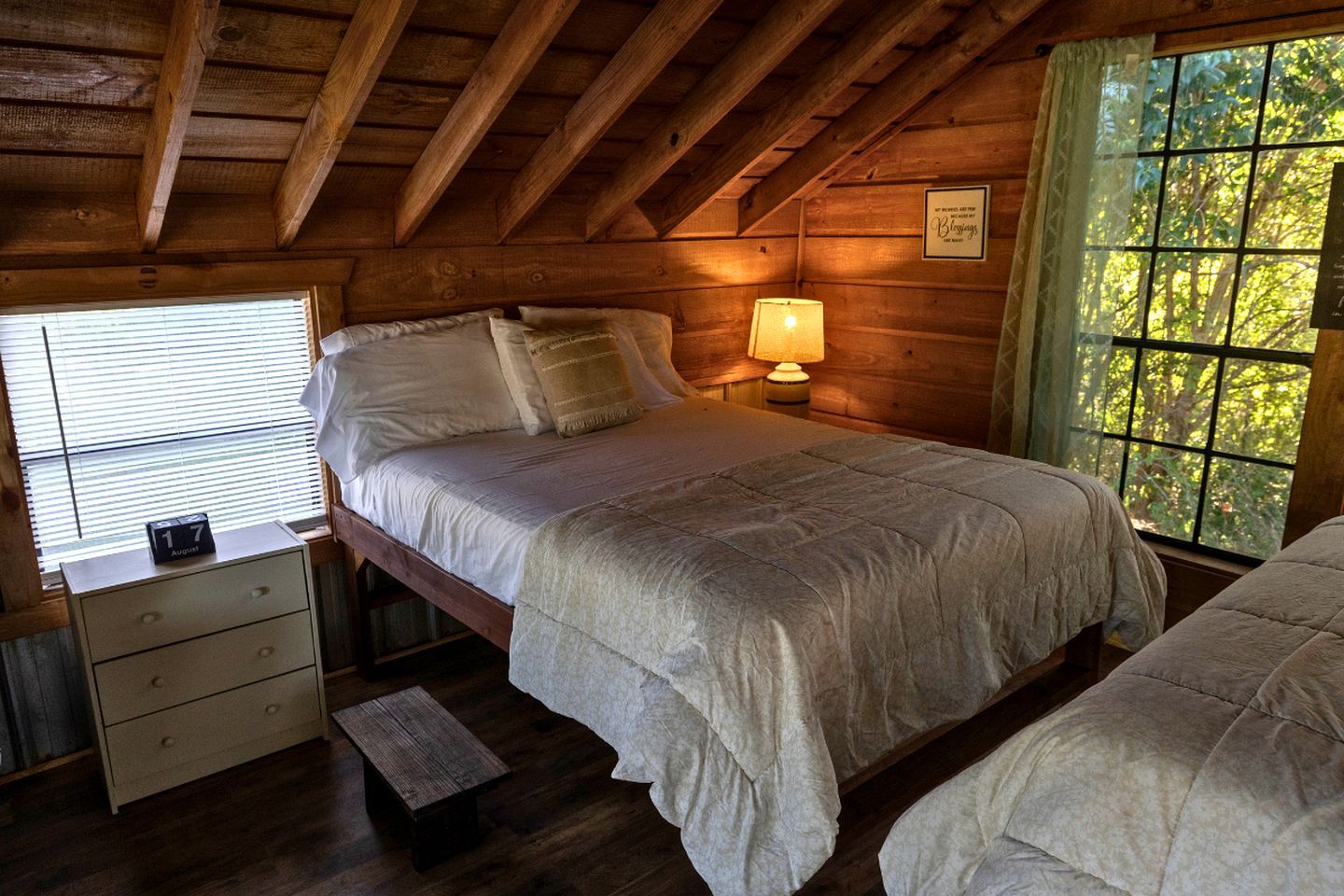 Une chambre à coucher dans un chalet en bois, avec un lit, une table de chevet et une fenêtre donnant sur la forêt.