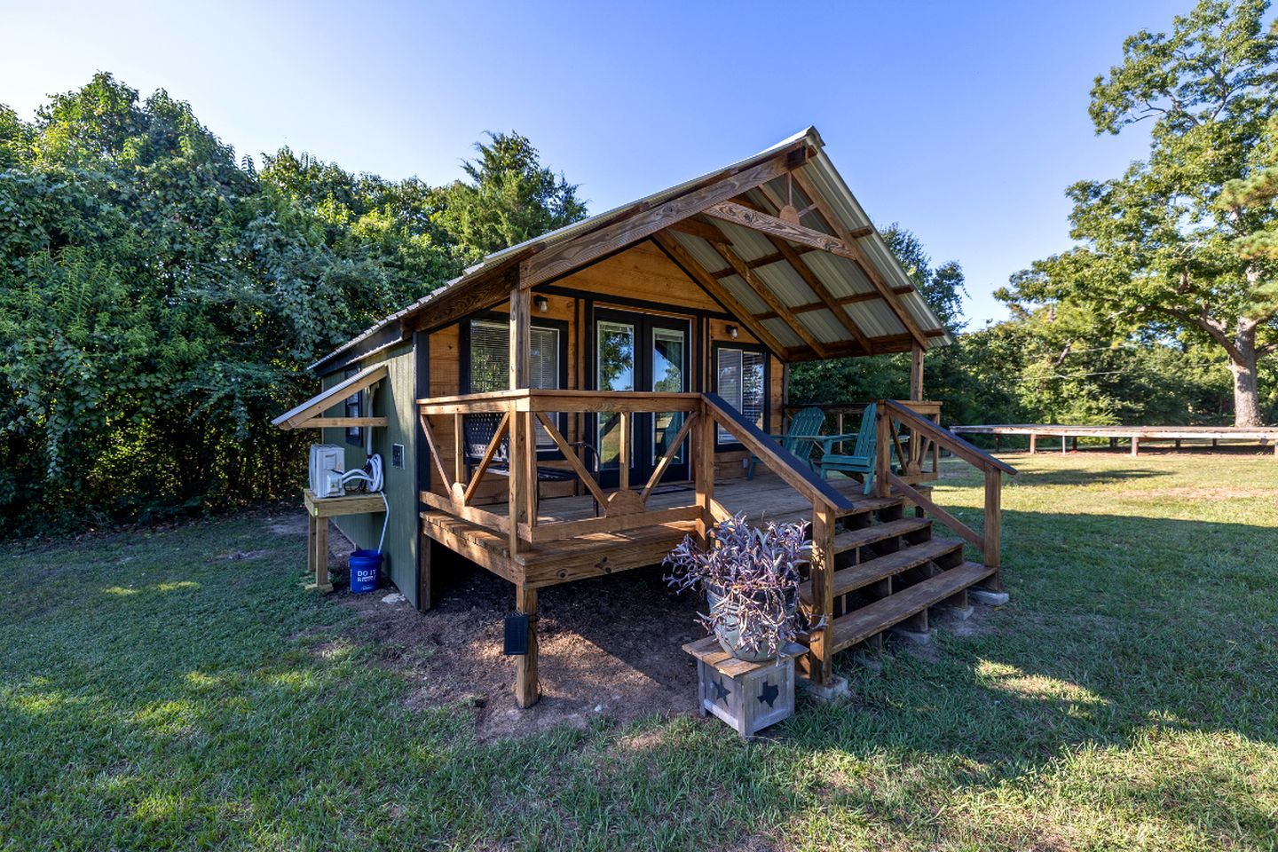A wooden cabin with a porch, a small deck, and a fenced yard.