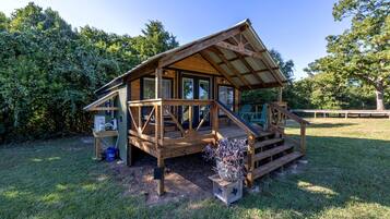A wooden cabin with a porch, a small deck, and a fenced yard.