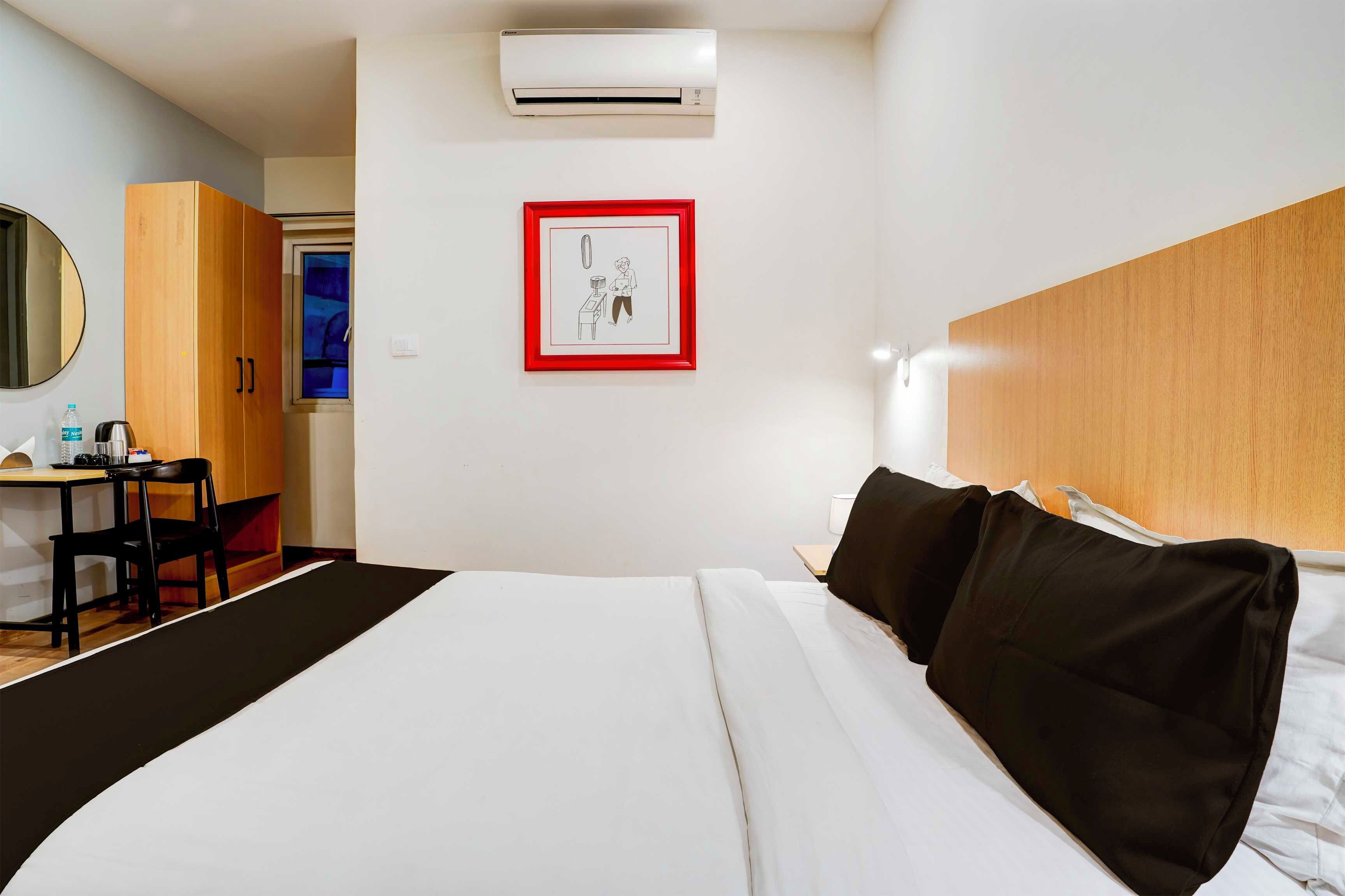 Habitación de hotel con cama, escritorio, silla, espejo y aire acondicionado de pared.