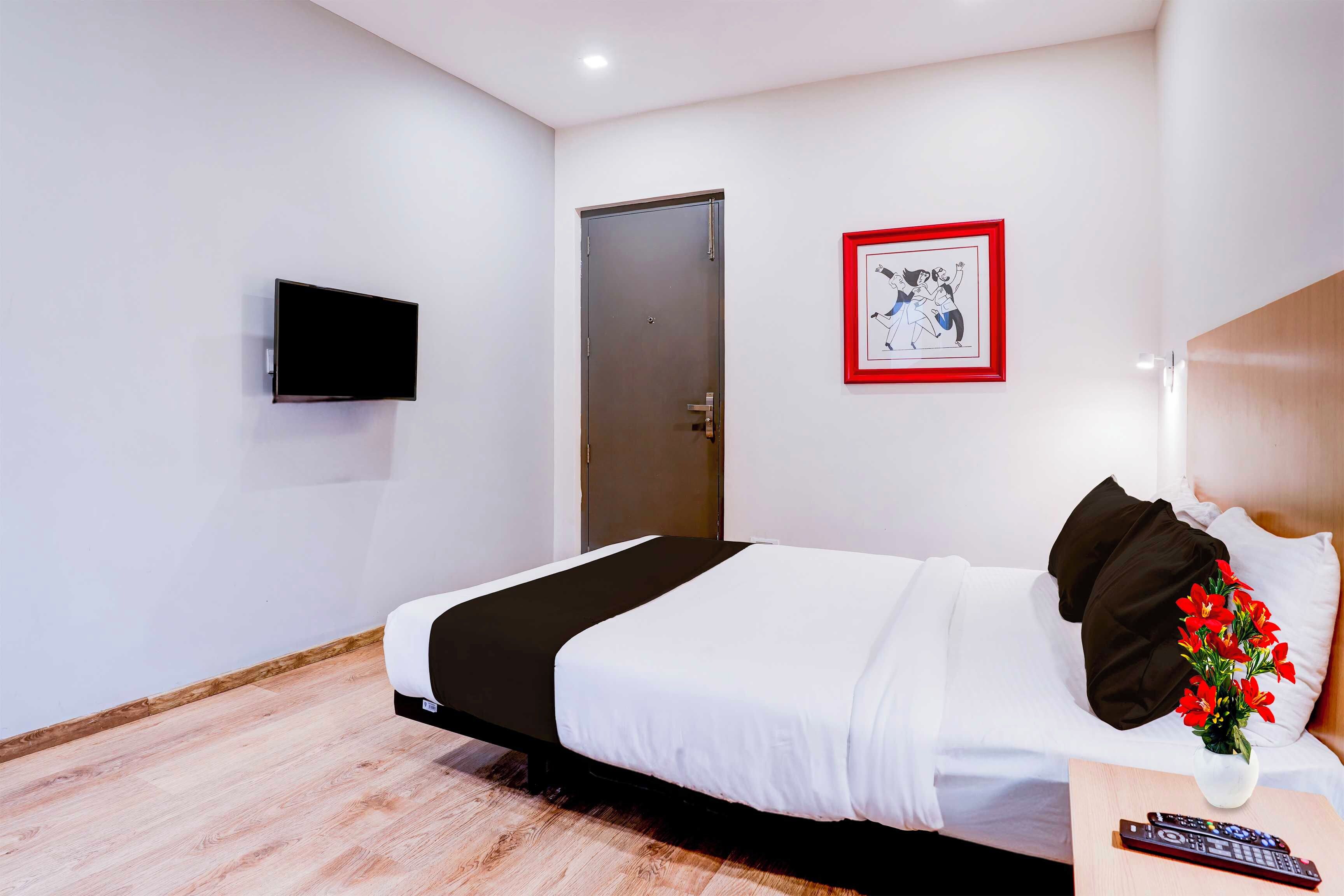 Habitación de hotel con una cama, un televisor de pantalla plana en la pared, una puerta y un cuadro enmarcado.