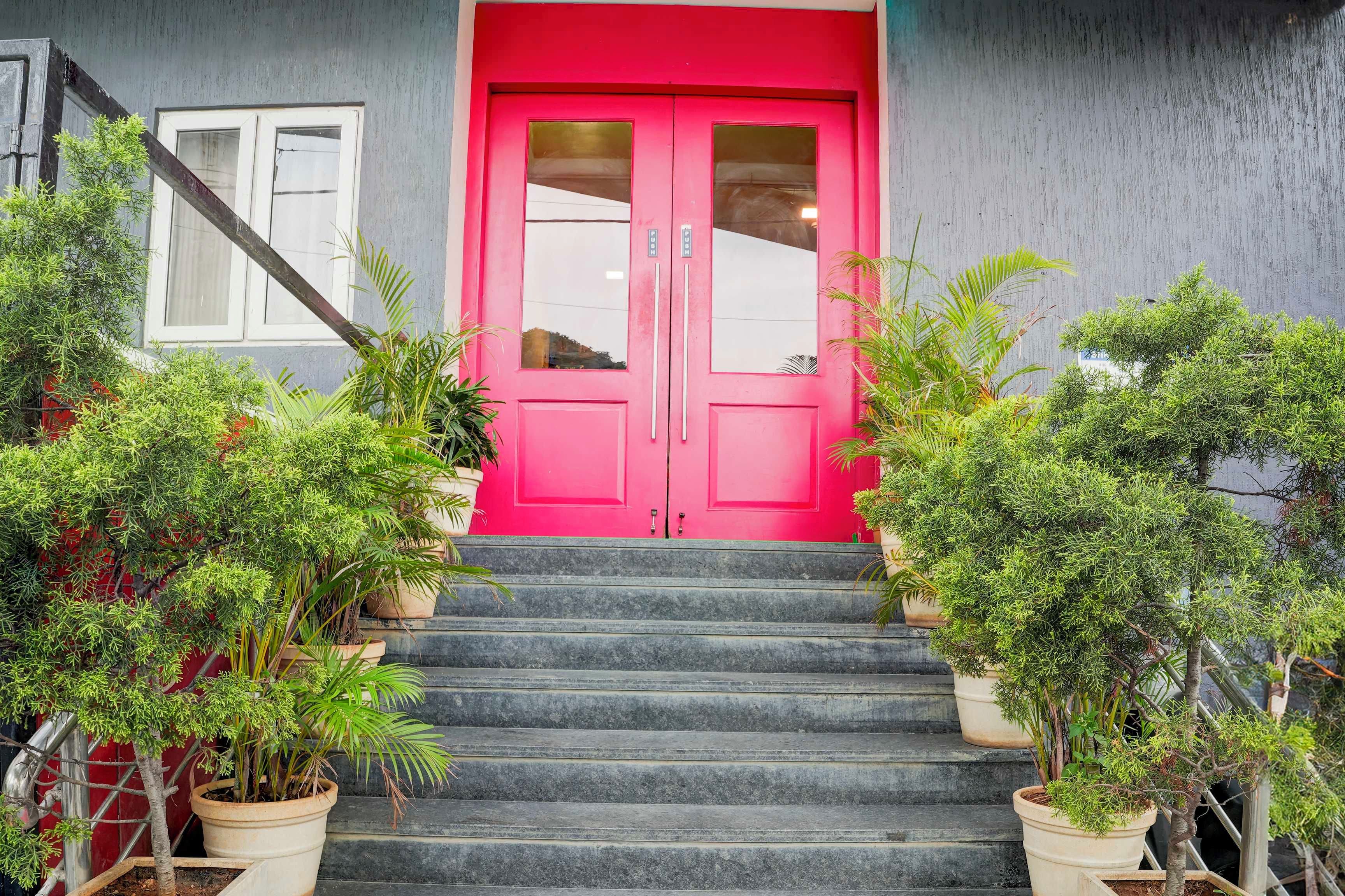 Un edifici amb una porta de color rosa viu, una escala que condueix a l'entrada i plantes en testos a banda i banda.