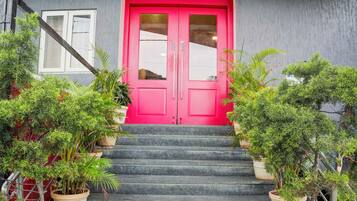Un edifici amb una porta de color rosa viu, una escala que condueix a l'entrada i plantes en testos a banda i banda.