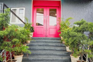 A building with a bright pink door, a staircase leading to the entrance, and potted plants on either side. - Townhouse Oak Bangalore Trinity (Bangalore)