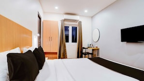 Ein Hotelzimmer mit einem Bett, einem Schreibtisch, einem Sessel, einem Fernseher und einem Fenster mit Vorhängen.