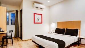 Ein Hotelzimmer mit Bett, Schreibtisch, Stuhl, Nachttisch, Lampe und Klimaanlage.
