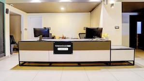 Un mostrador de recepción con un cartel que indica servicio de empresa. Hay dos monitores de computadora, un teclado y un ratón en el mostrador. Una silla se encuentra a la izquierda del mostrador.