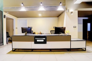 Un mostrador de recepción con un cartel que indica servicio de empresa. Hay dos monitores de computadora, un teclado y un ratón en el mostrador. Una silla se encuentra a la izquierda del mostrador.