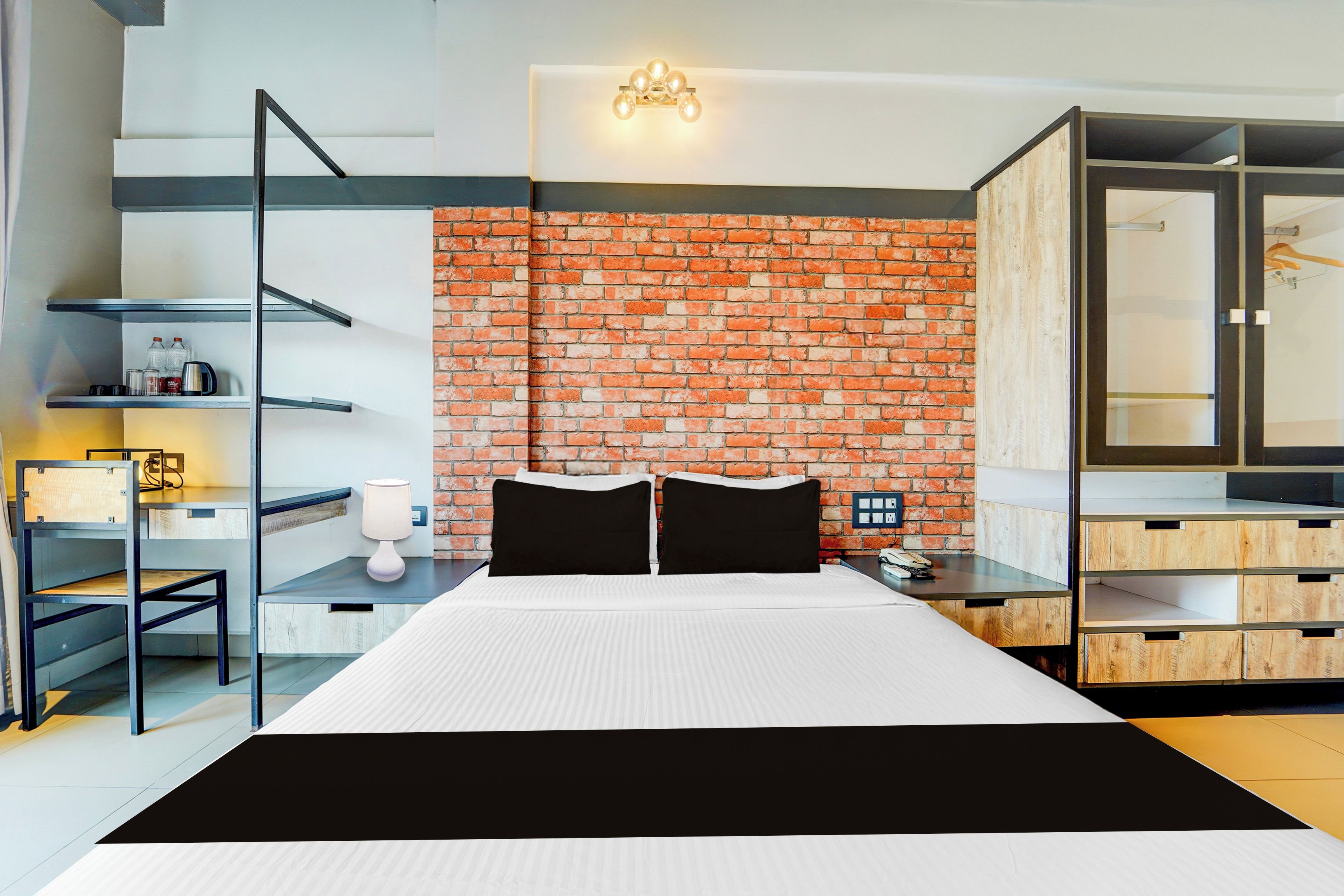Een moderne hotelkamer met een bakstenen muur, een bed met zwart-wit beddengoed, een bureau met een lamp en een kledingkast.