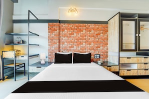 Una habitación de hotel moderna con una pared de ladrillo, una cama con ropa de cama blanco y negro, un escritorio con una lámpara y un armario.