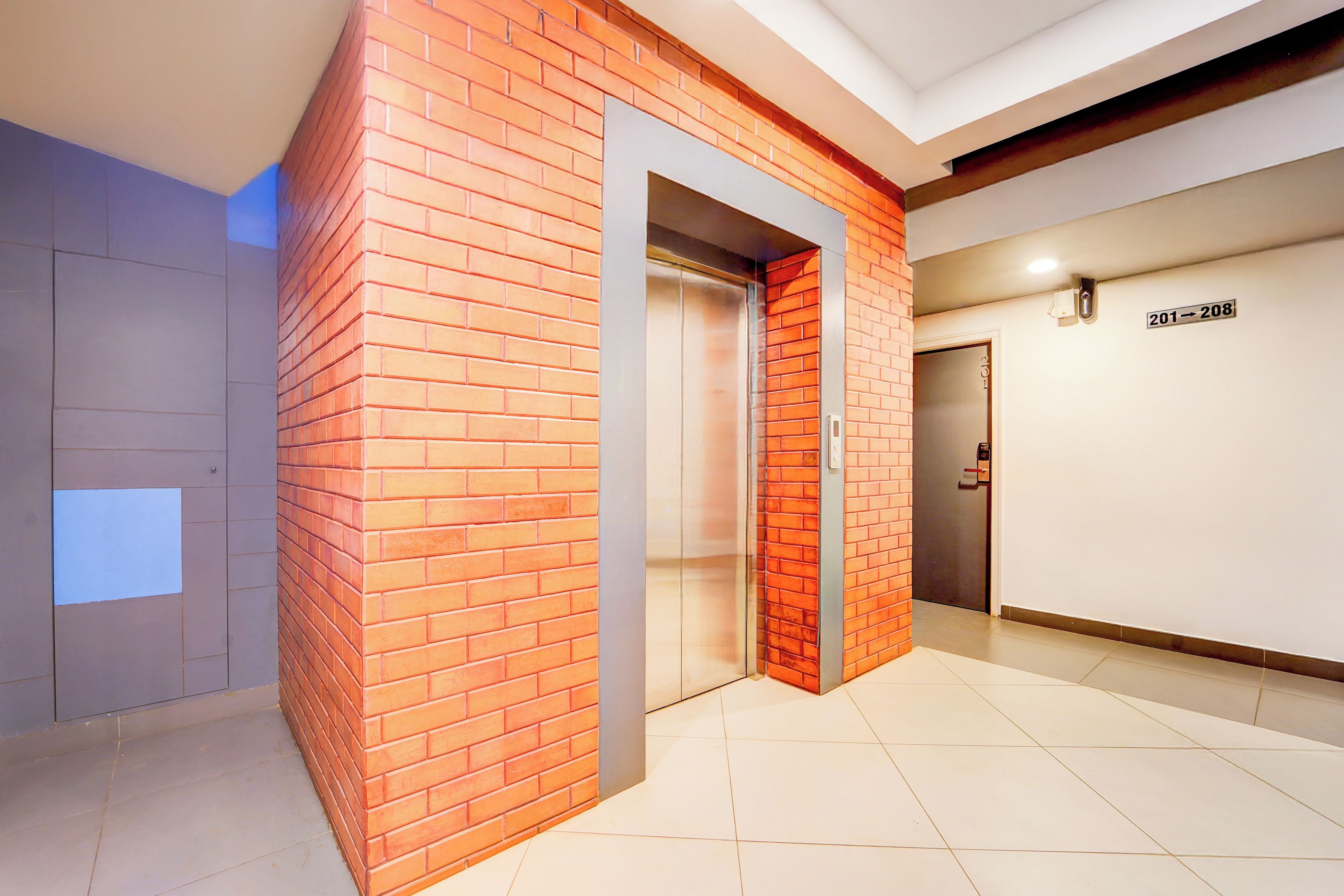 A modern elevator with a brick facade, a clear glass elevator door, and a sign indicating floor numbers 201-208.