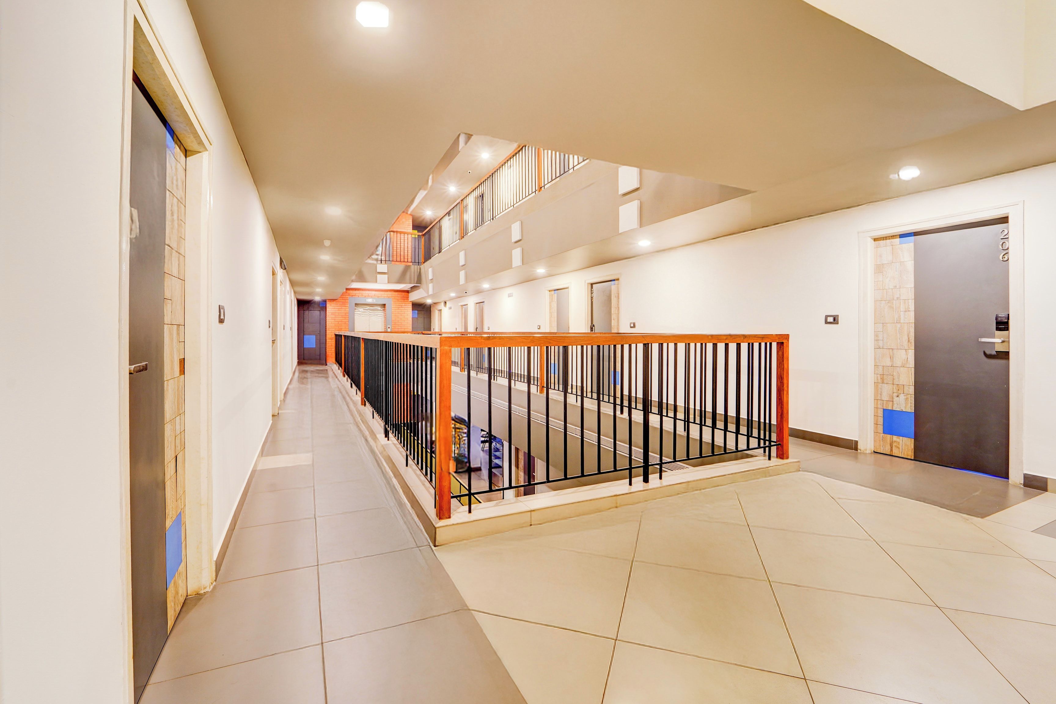 Pasillo de hotel de varios niveles con suelo de baldosas, barandilla metálica y puertas que dan a habitaciones.