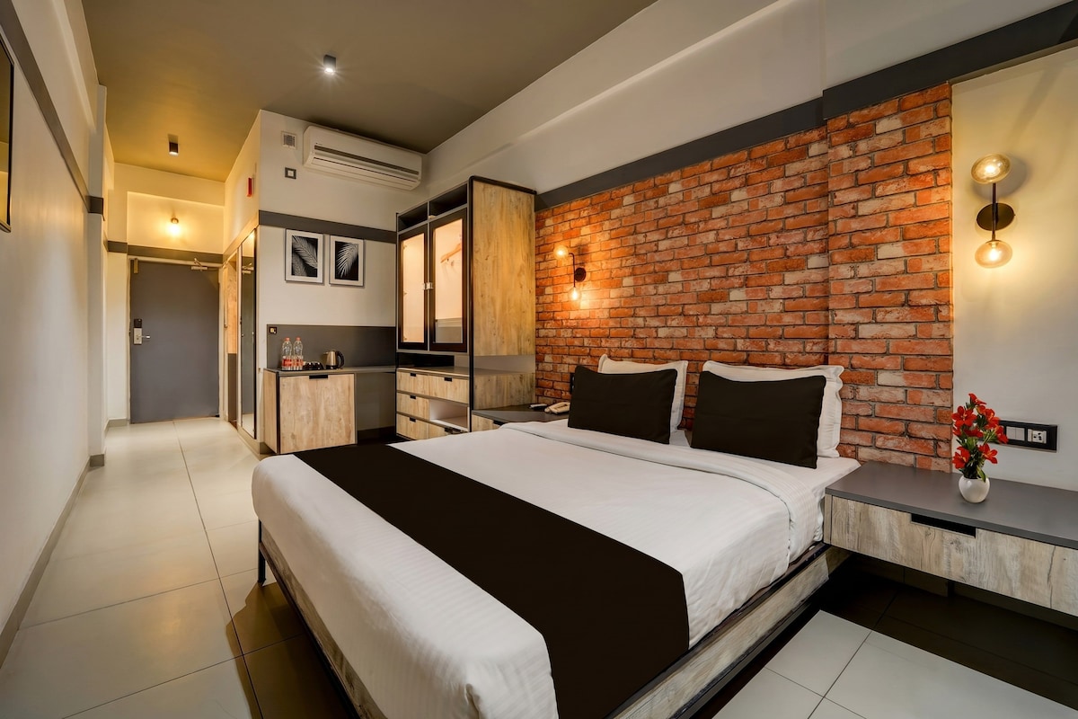Habitación de hotel moderna con pared decorada en ladrillo, una cama grande con ropa de cama blanco y negro, una mesita de noche con un jarrón de flores y un armario empotrado con espejo.