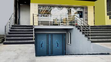 Rakennuksessa on portaikko, joka johtaa toisen kerroksen sisäänkäyntiin, sininen ovi, jossa on riikinkukon kuva, ja keltainen seinä.