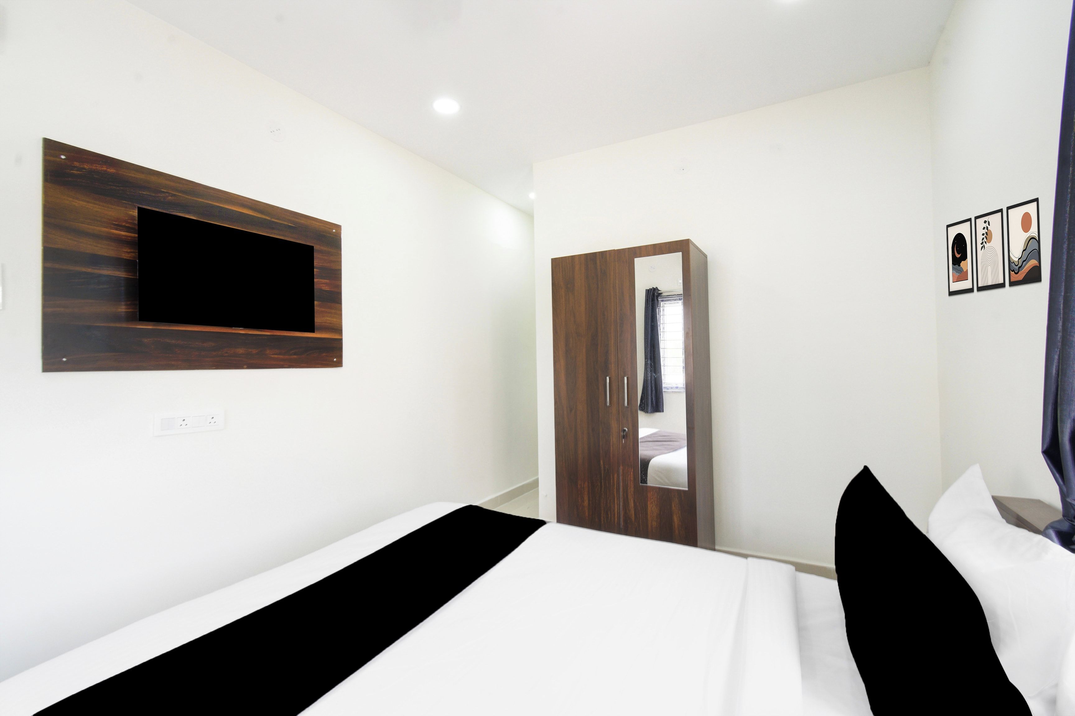 A bedroom with a bed, a wardrobe, a mirror, and a wall-mounted TV.