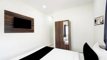 A bedroom with a bed, a wardrobe, a mirror, and a wall-mounted TV.