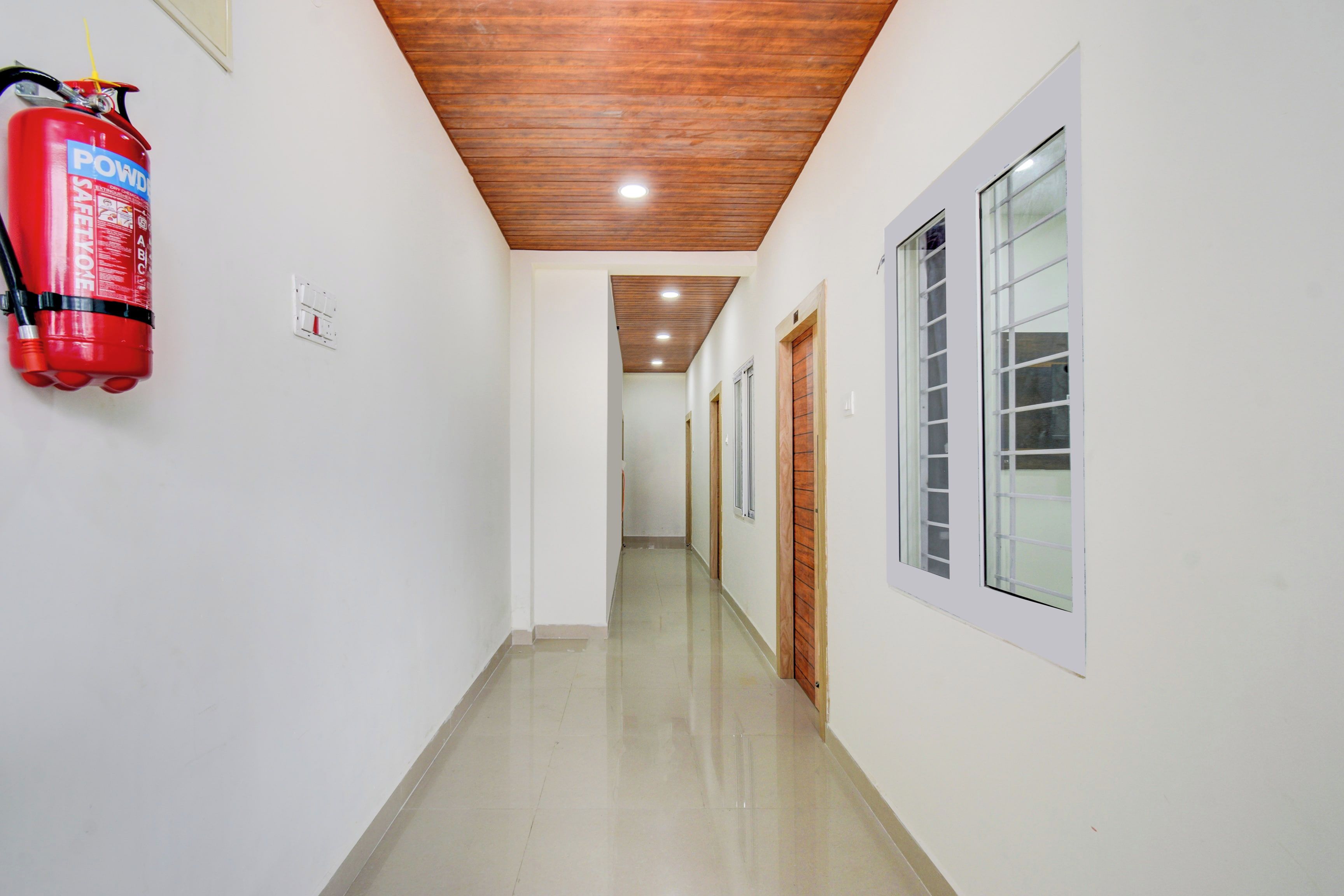 A hallway with a fire extinguisher mounted on the wall, wooden ceiling, and doors leading to rooms.