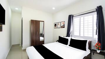 A hotel room with a bed, a wardrobe, a window with curtains, and a wall-mounted TV.