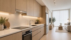 Cozinha moderna com eletrodomésticos embutidos, sala de jantar com sofá e uma janela grande com persianas.