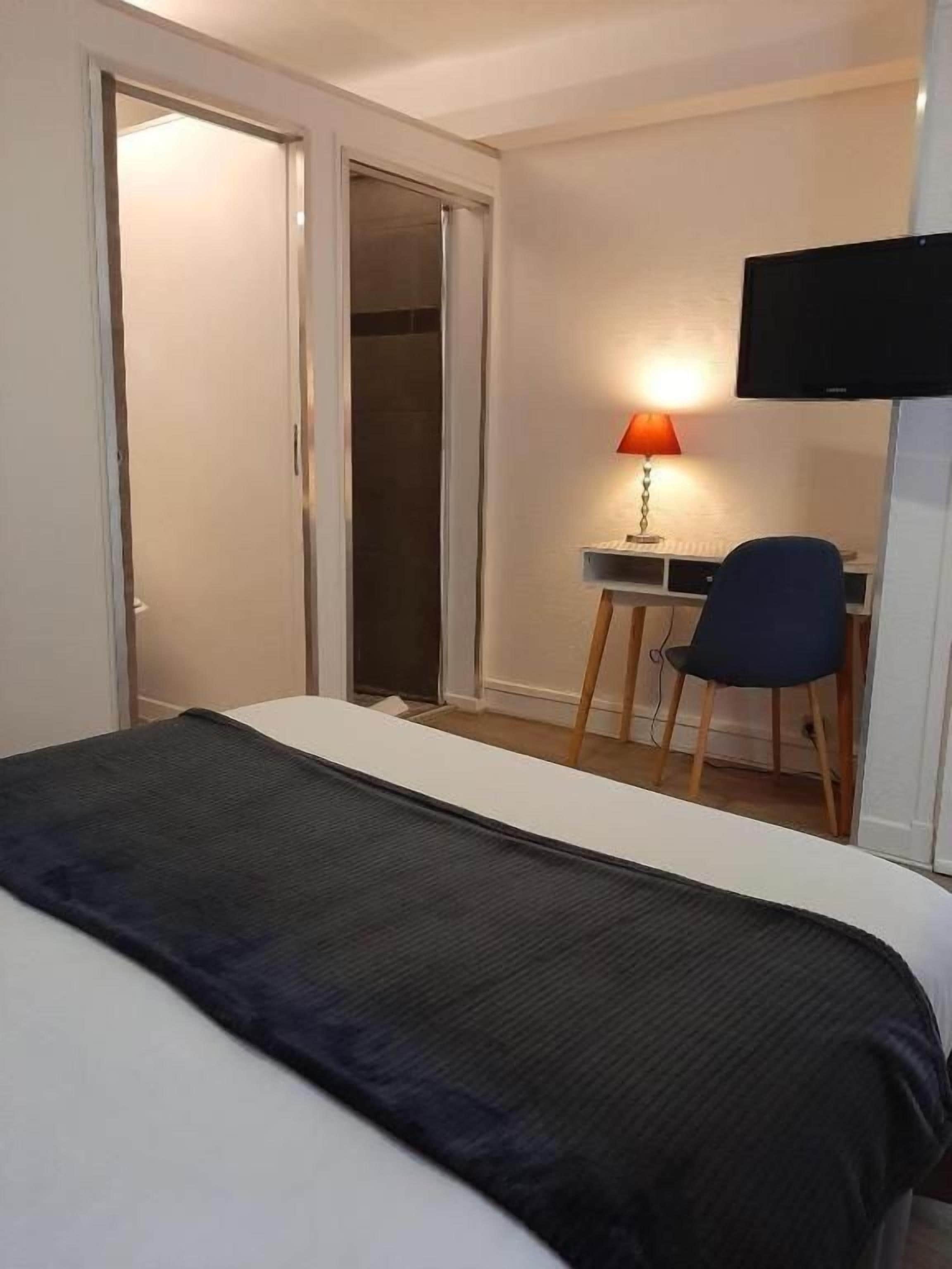 Habitación de hotel con una cama, un escritorio con una silla, un televisor y una puerta corrediza.