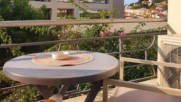Een balkon met een ronde tafel, een stoel en een gebouw op de achtergrond.