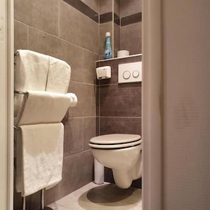 Un baño con inodoro, toallero y repisa con artículos de aseo.