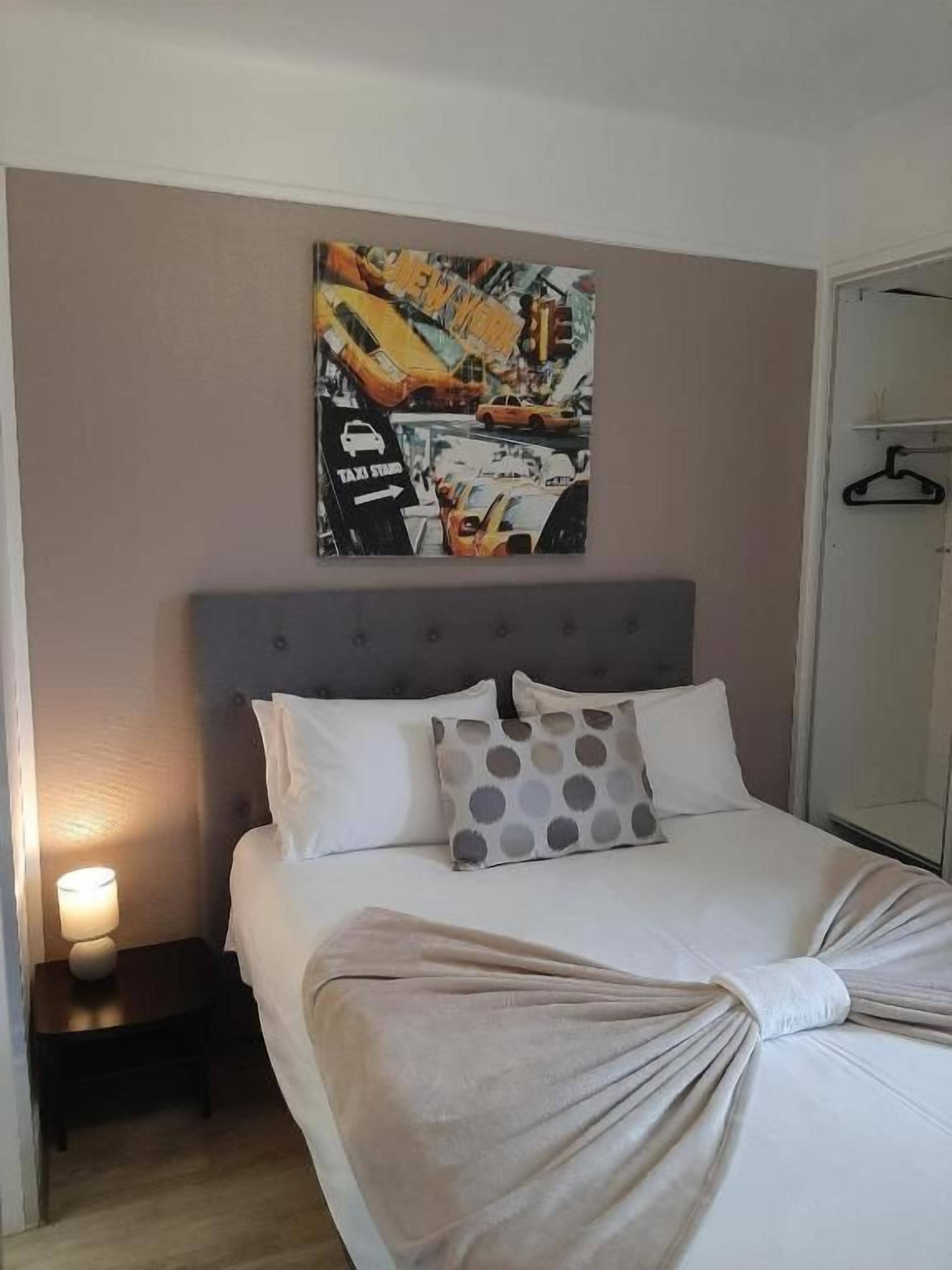 Una habitación de hotel con cama, mesita de noche, un cuadro en la pared y un armario.