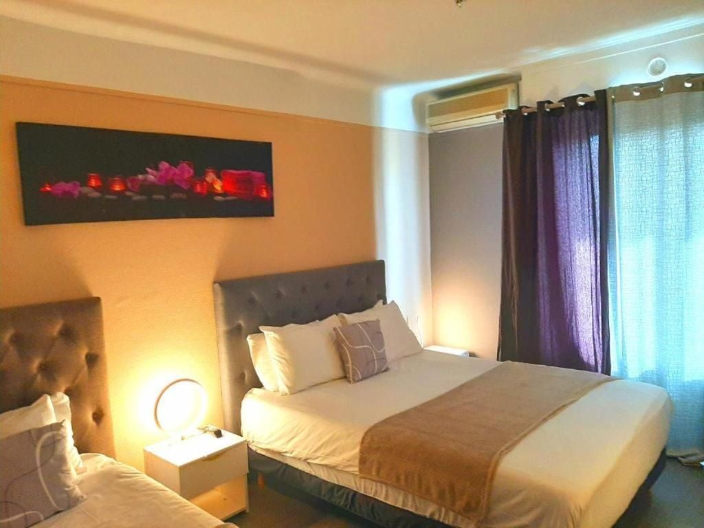 Habitación de hotel con una cama grande, una mesita de noche con lámpara, una obra de arte en la pared y una ventana con cortinas.