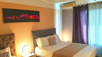 Habitación de hotel con una cama grande, una mesita de noche con lámpara, una obra de arte en la pared y una ventana con cortinas.