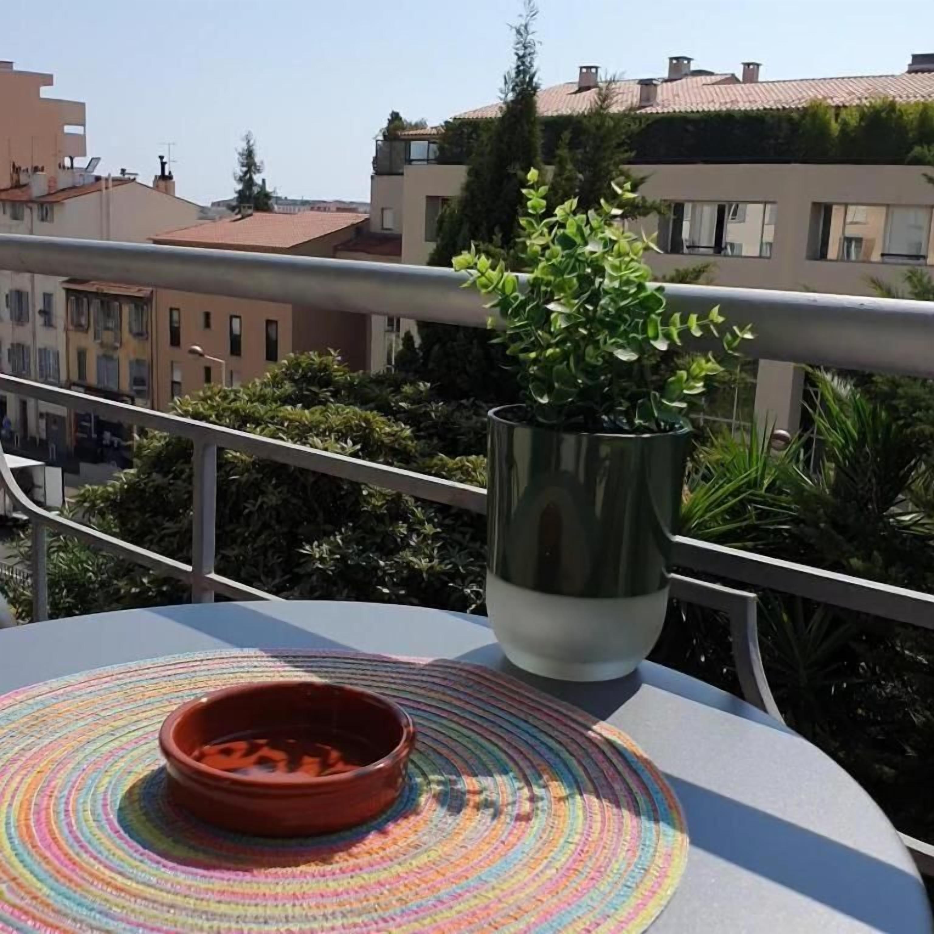 Ein Balkon mit einem Blumentopf, einer farbenfrohen gewebten Unterlage und einer Terrakotta-Schale.