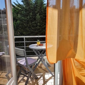 A balcony with a table and chairs, a glass door, and a view of trees.