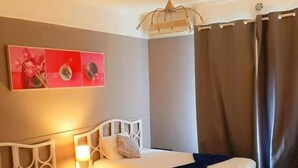 Een hotelkamer met twee bedden, een nachtkastje met een lamp, een wanddecoratie en een raam met gordijnen.