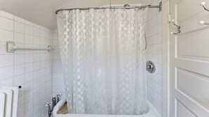 Een badkamer met een witte badkuip, een douchegordijn en een witte deur.