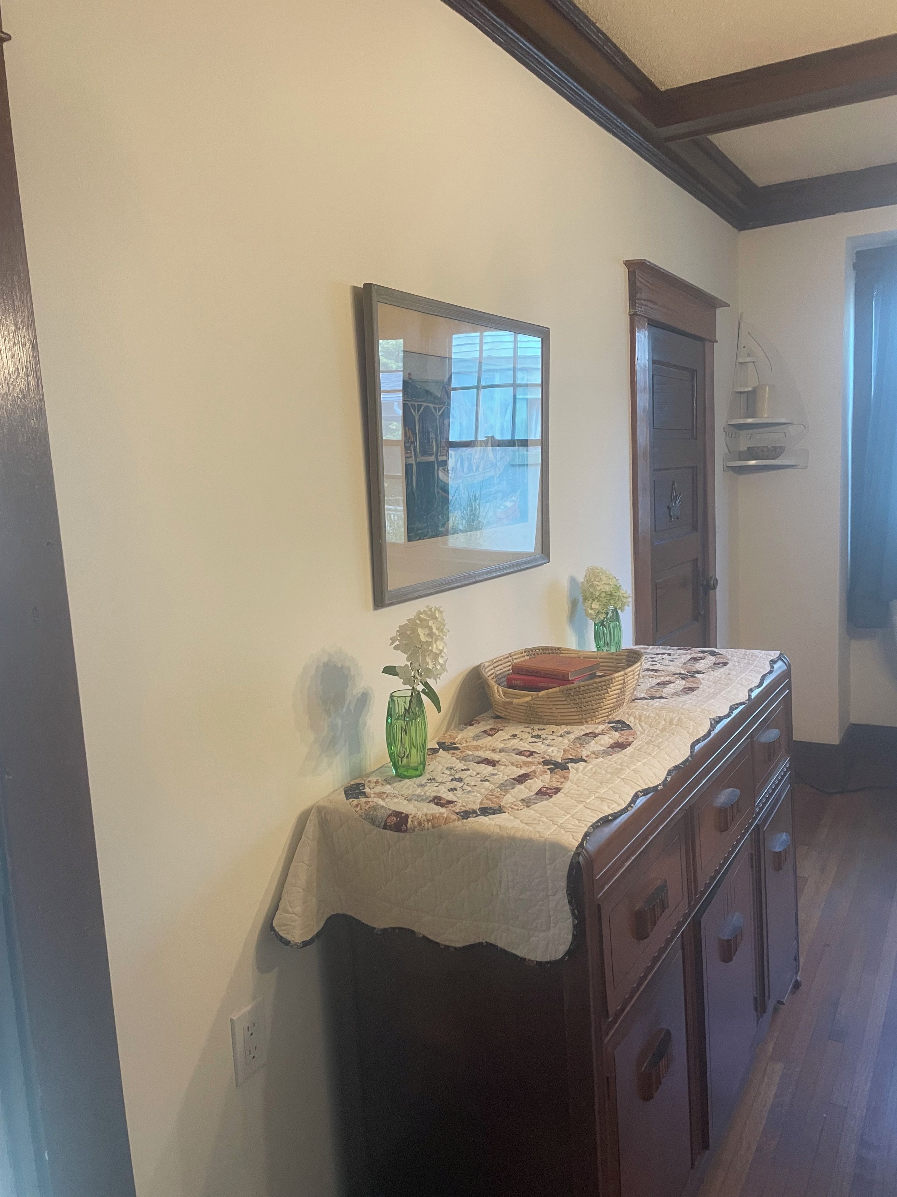 A room with a wooden dresser, a mirror, a vase with flowers, and a quilted tablecloth.