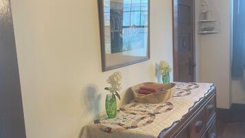 A room with a wooden dresser, a mirror, a vase with flowers, and a quilted tablecloth.