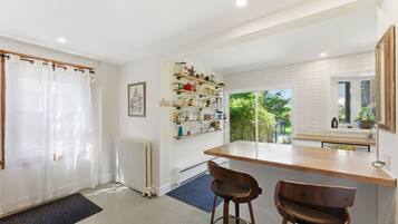 A modern kitchen with a wooden countertop, two bar stools, a radiator, and a window with a view of greenery.
