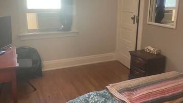 A room with a bed, a desk, a dresser, a window with curtains, and a mirror on the wall.