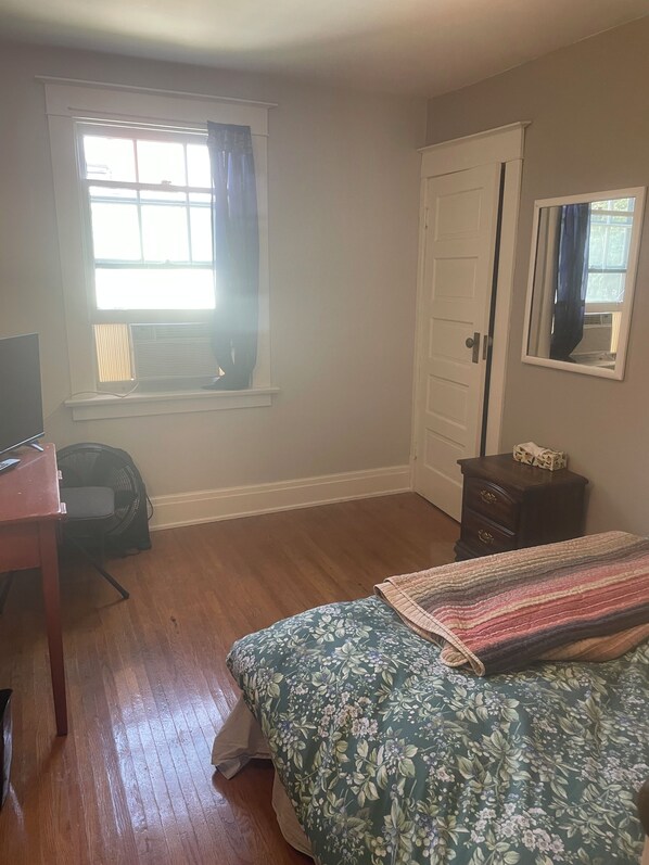 A room with a bed, a desk, a dresser, a window with curtains, and a mirror on the wall.