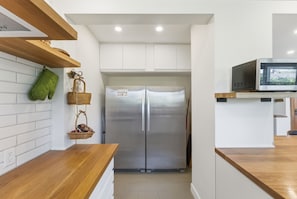 A kitchen with a stainless steel refrigerator, wooden countertops, and a microwave on an open shelf.