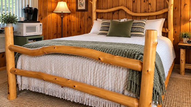 Quarto com painéis de madeira, uma cama, luminária de cabeceira, micro-ondas e um quadro na parede.
